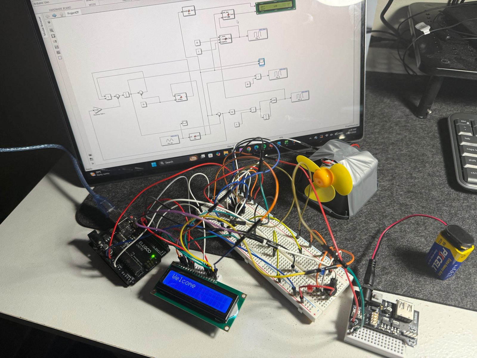 The thermal digital twin rig on a desk with the Simulink model open on the monitor behind it